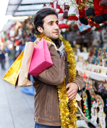 Smiling man with garland choosing decorations at Christmas marketの写真素材