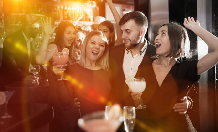 Happy young man with female friends enjoying cocktail party in bar