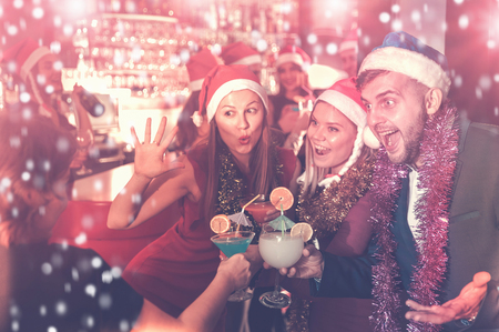 Young man and two women with cocktails in Santa hats celebrating at nightclubの写真素材