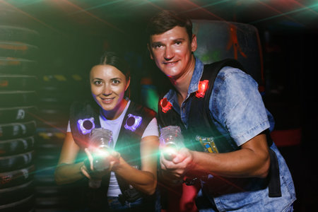 happy couple holding colored laser guns during laser tag game in labyrinth