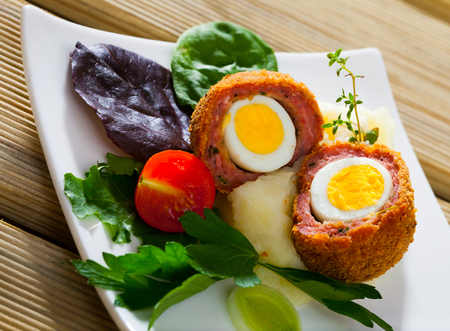 Hard-boiled quail egg wrapped in sausage meat, breaded and fried (Scotch egg) served with pureed potatoes, baked carrots, cherry tomatoes and greensの写真素材
