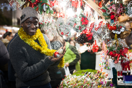 Smiling African American man selecting festive home decoration at outdoor Christmas fairの写真素材