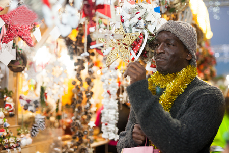 Smiling African American man selecting festive home decoration at outdoor Christmas fairの写真素材
