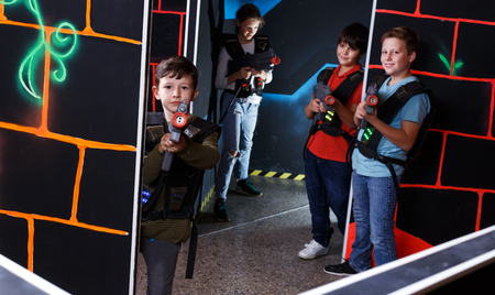 Excited active young boy aiming laser gun at other players during lasertag game in dark roomの写真素材