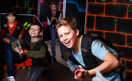 Portrait of happy cheerful preteen boy with laser gun having fun on dark lasertag arenaの写真素材