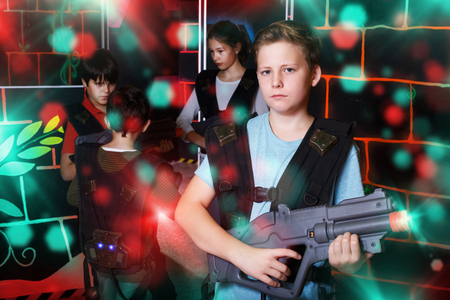 positive teen boy standing with laser pistol in dark lasertag room during game with friendsの写真素材