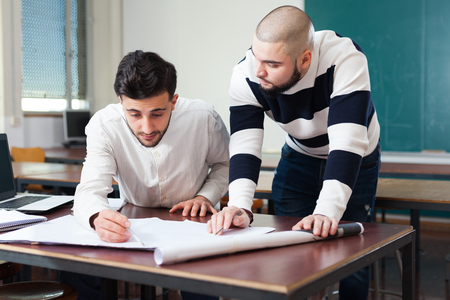 Two male university students sitting at desk preparing for exams together in classroomの写真素材