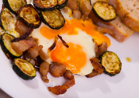 Close up of  cooked scrambled  eggs with zucchini and fried lard at plate on tableの写真素材