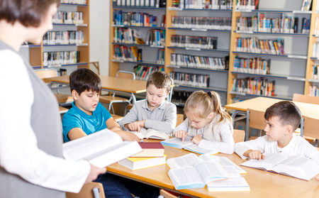 Portrait of young female librarian and diligent schoolkids during classes in school libraryの写真素材