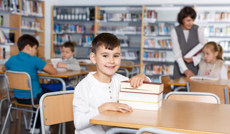 Portrait of smiling preteen boy sitting with pile of textbooks in school libraryの写真素材