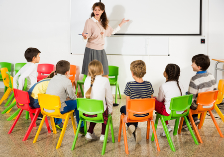 Portrait of young female teacher conducting lesson for small school children, listening attentively to herの写真素材