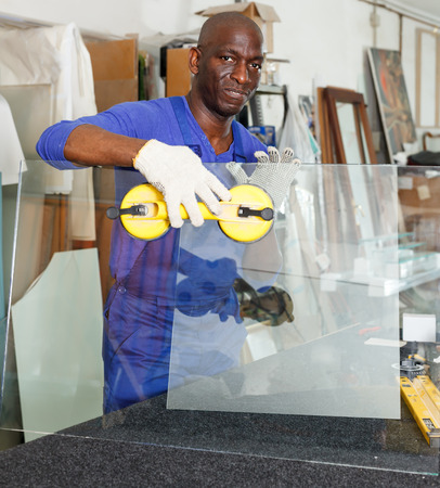 Cheerful experienced glazier during daily work in glass factoryの写真素材