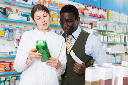 Young woman explaining prescribed medicine to African American man in pharmacyの写真素材