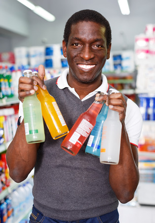 Positive African man choosing energy drinks in supermarketの写真素材