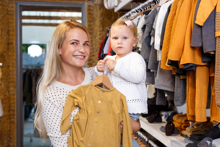 Cheerful young woman and her little daughter shopping in kids clothing storeの写真素材