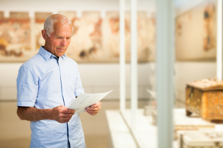 Attentive mature man exploring artworks in glass case in museumの写真素材