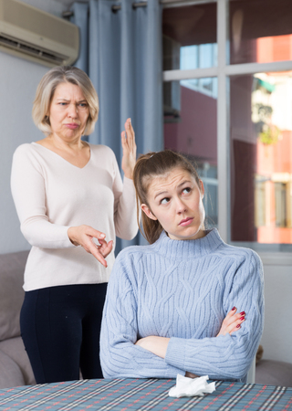 Mature woman scolding her upset adult daughter at home interiorの写真素材