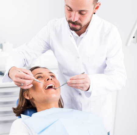 Dentist is treating female patient which is sitting in dental chair in clinicの写真素材