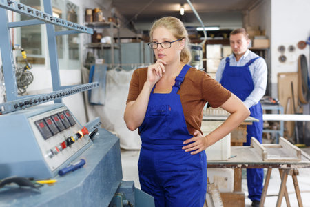 Confident female glazier working on glass straight line bevelling machine in workroom