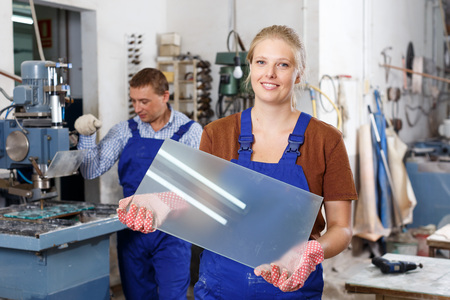 Portrait of successful female glazier posing in glass factory with glass in handsの写真素材