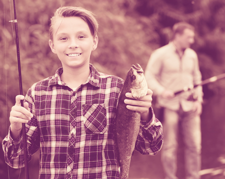 Smiling teenage boy holding catch freshwater fish in handsの写真素材