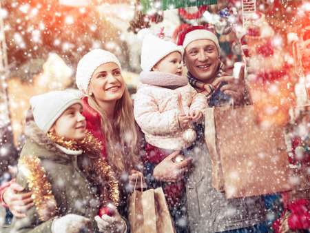 Smiling parents with their two nice daughters choosing Christmas toys at Christmas fairの写真素材