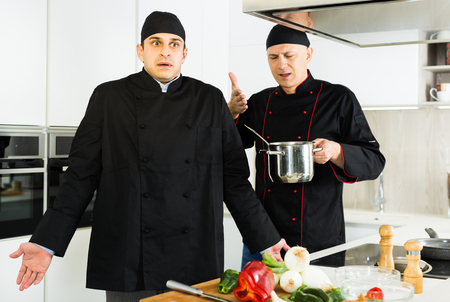 Professional men chefs  in black uniform having conflict  on kitchenの写真素材