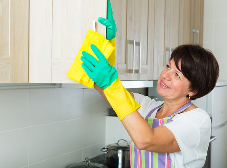 glad retiree woman cleaning surfaces at home using duster and household chemicalsの写真素材