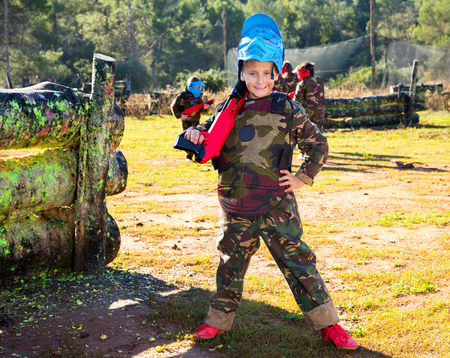 Happy positive  boy paintball player in camouflage standing with gun before playing outdoorsの写真素材