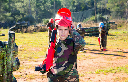 Positive smiling boy paintball player in camouflage standing with gun before playing outdoorsの写真素材