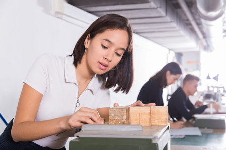 Female student of faculty of architecture engaged in architectural modeling in university studio