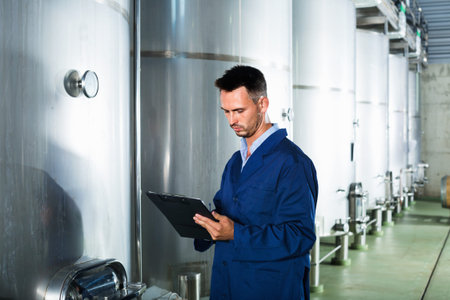Portrait of  diligent man wearing coat taking off data from equipment in winery fermentation section