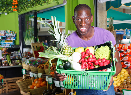 Portrait of glad  positive  man who is standing with basket with fruits in the market.の写真素材