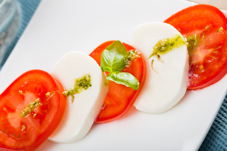 Mediterranean food, caprese salad - tomatoes, mozzarella cheese, basil and pesto on white plateの写真素材