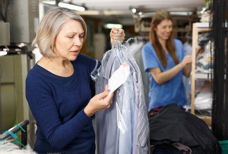 Portrait of cheerful female laundry customer holding clean clothes on hangerの写真素材