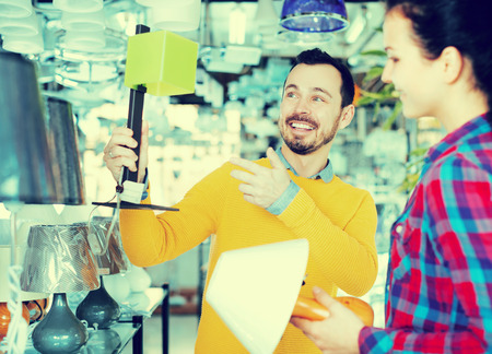 Adult man and girl in lighter shop choose table lamp for houseの写真素材
