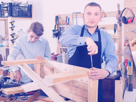 happy european  father and son repairing wood bench at garageの写真素材