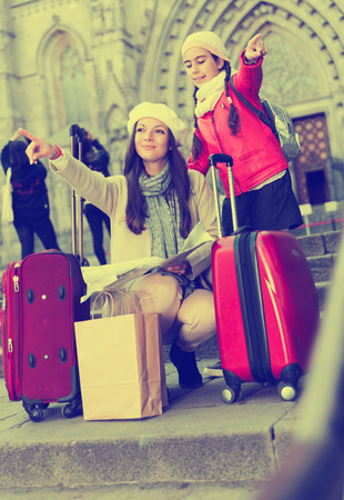 Cheerful girl and woman with map in scarf and hat in autumn seasonの写真素材