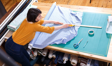 High angle view of female seller of fabric shop measuring and cutting off piece of textile for...