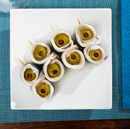 Top view of savory rolls of marinated herring fillet with olives stuffed with paprika served on white plateの写真素材
