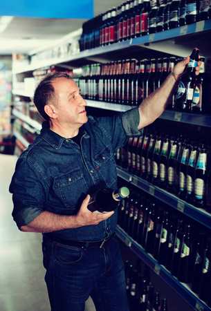 Portrait of a happy smiling glad elderly man buying a beer at the grocery storeの写真素材