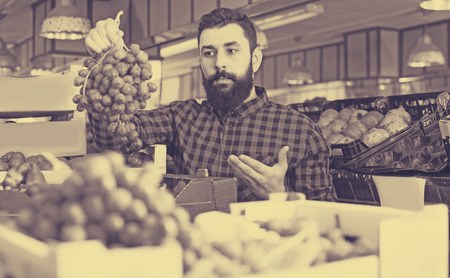 Positive man seller choosing  grapes in grocery shopの写真素材