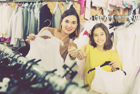 Smiling young mother and daughter showing their purchases in childrenâs cloths shopの写真素材