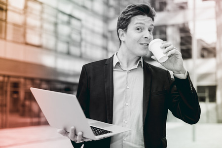 Cheerful  businessman with laptop and coffee standing in the streetの写真素材