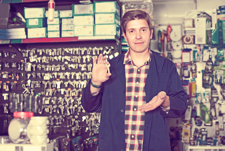 Cheerful germany worker in hardware store trading goods and keys in uniformの写真素材