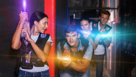 Portrait of happy cheerful  smiling young friends playing laser tag  game  with laser guns in dark corridorの写真素材