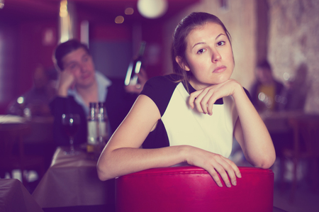 Portrait of upset young woman on background with drunk man at restaurant tableの写真素材