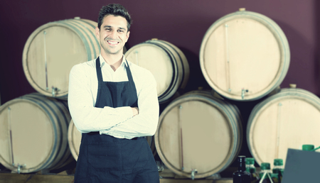 Smiling professional man seller in uniform standing in shop with wine woodsの写真素材