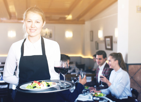 Portrait of smiling waitress with serving tray meeting restaurant guestsの写真素材