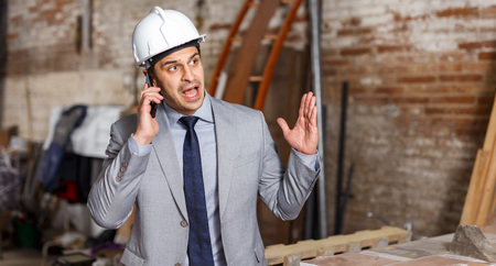 Unhappy male architect talking on phone during supervising buildingの写真素材